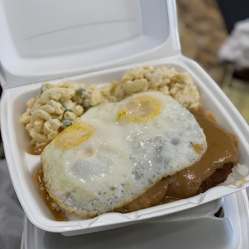 Hawaiian Loco Moco with two fried eggs, gravy, and macaroni salad in a takeout container.