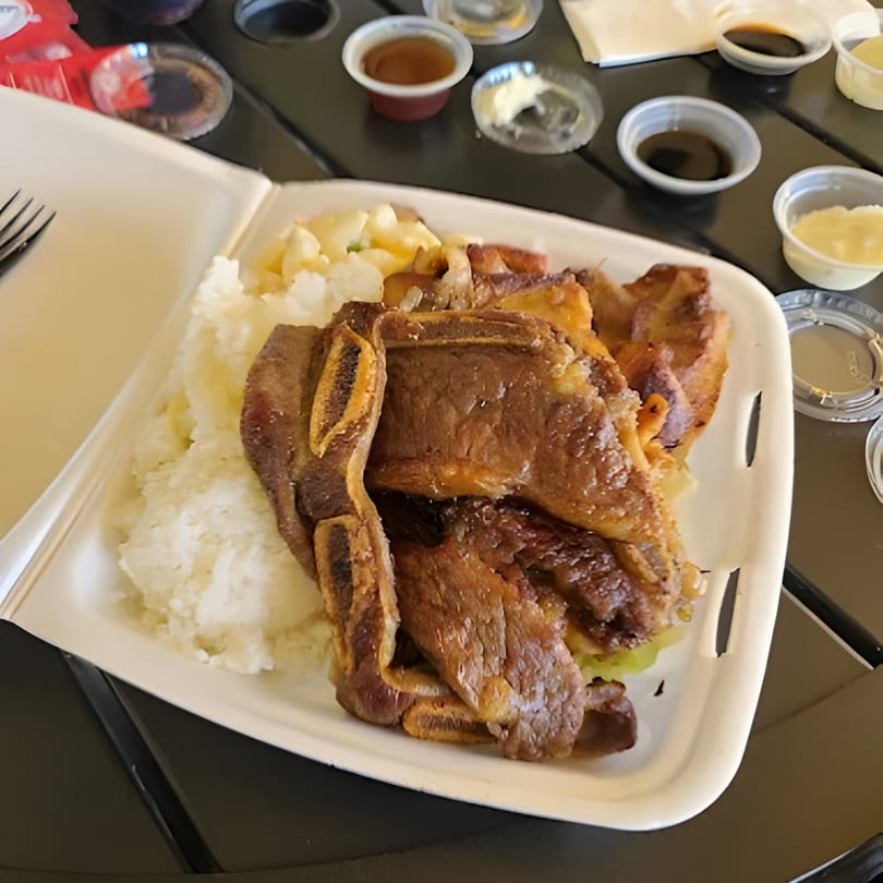 Hawaiian BBQ short ribs with rice and macaroni salad in a takeout container, with sauces.